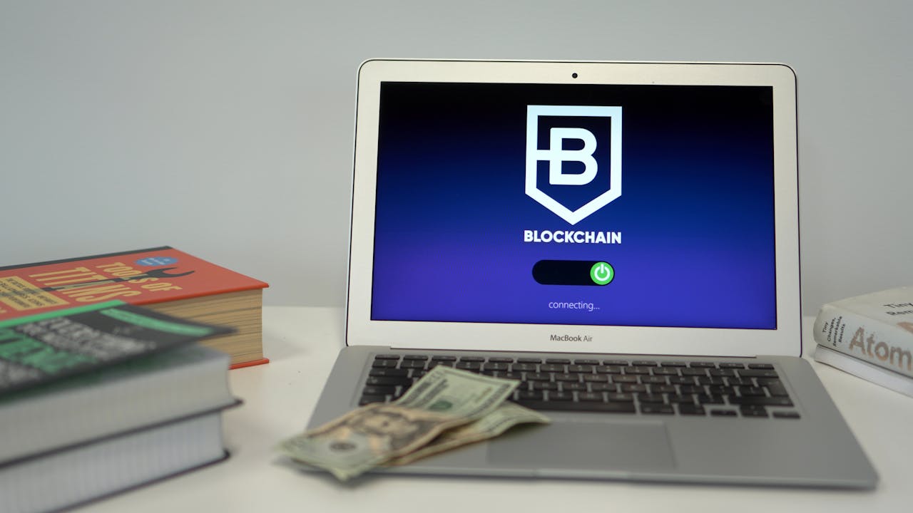Laptop showing blockchain connection screen on desk with books and US dollars.